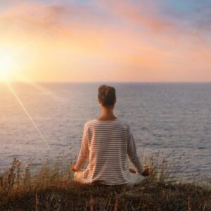 Person meditating on a mountain, symbolizing deep relaxation and self-compassion.