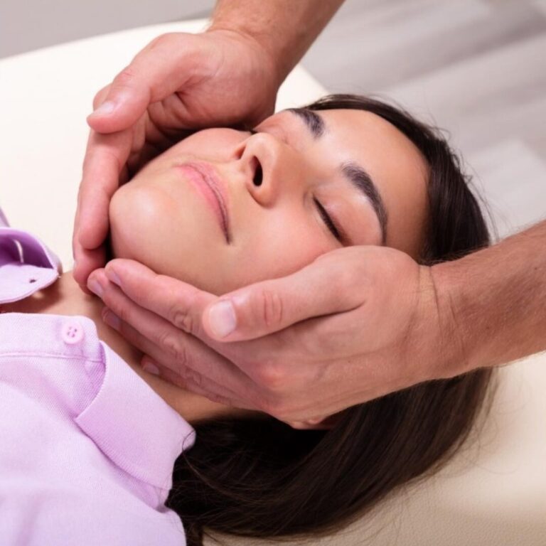 Woman relaxing while a therapist gently massages her jaw to relieve tension.