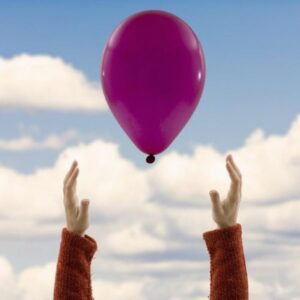 Hand releasing a balloon into the clear sky, symbolizing freedom and letting go.