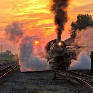 Vintage train moving through a misty countryside at dawn with smoke rising from the engine