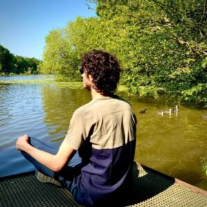 Man sitting peacefully by a calm lake, reflecting in stillness and serenity