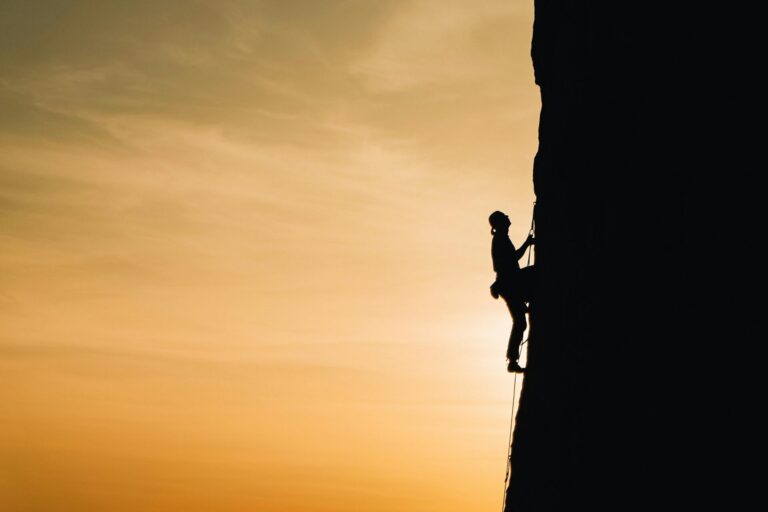 Person climbing a steep rock, symbolizing strength and determination in overcoming emotional challenges.