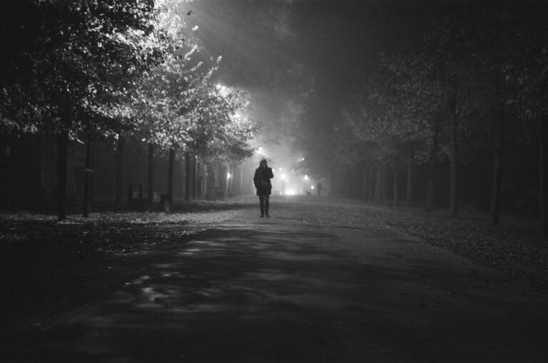 Person walking alone on a dark pathway toward the light, symbolizing hope and the journey from struggle to healing.