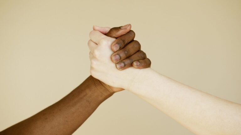 Black and white photograph of two hands holding together, symbolizing healing, solidarity, and resilience through racial trauma.