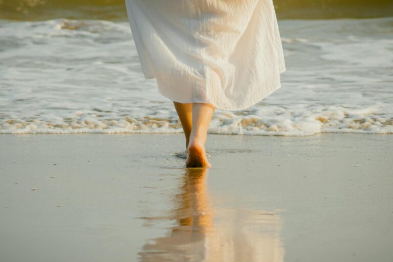 Person walking peacefully along the beach shoreline at sunset, symbolizing calm and reflection.”