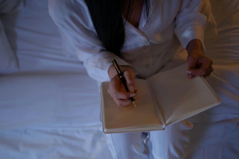 A woman writing in a journal at night before bed, reflecting after a busy day, symbolizing calm and self-care.