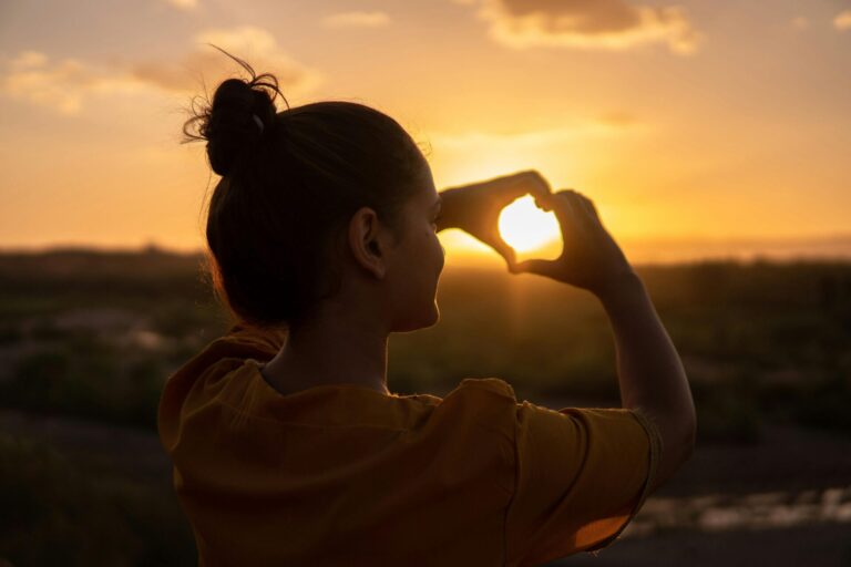 Hands forming a heart shape around a warm glowing light, symbolizing love toward self and others.