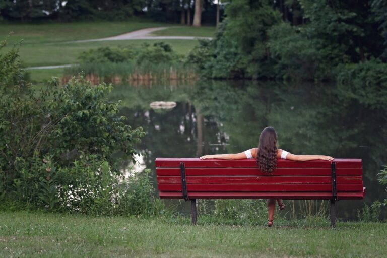 A woman resting in nature, surrounded by trees, head tilted back in quiet relief and calm.