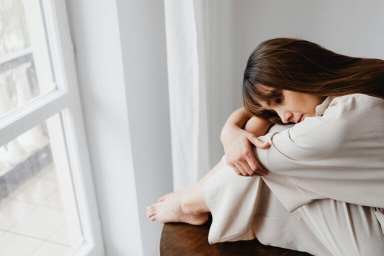 Woman sitting peacefully beside a window, bathed in sunlight, practicing relaxation for anxiety relief hypnosis.