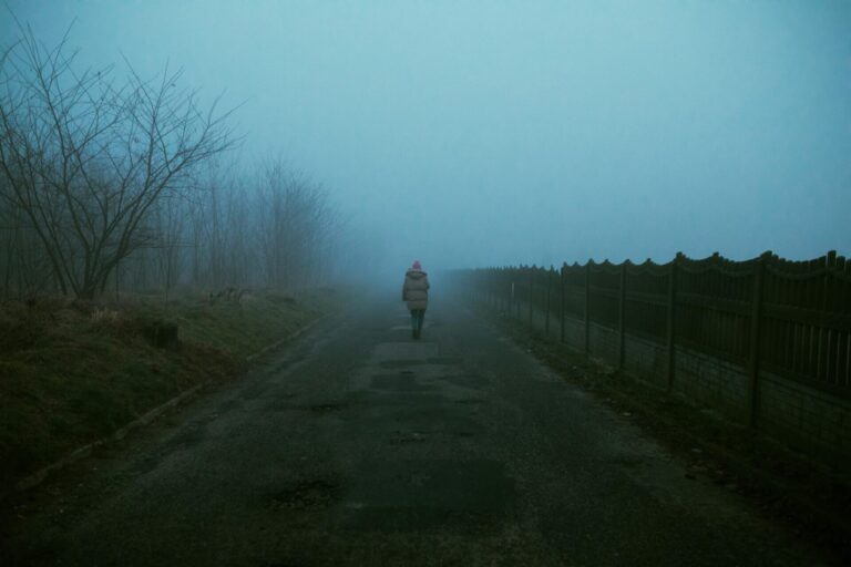 Person standing at a foggy crossroads or path, looking hesitant and contemplative, symbolizing uncertainty.