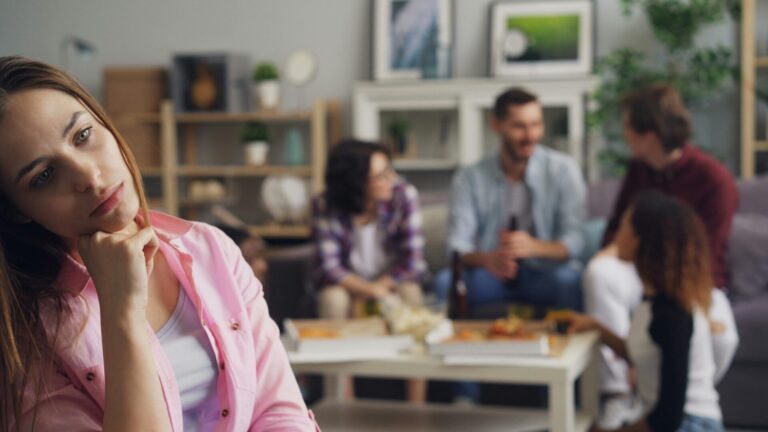 Person sitting or standing alone in a social setting, looking nervous, withdrawn, or uneasy.