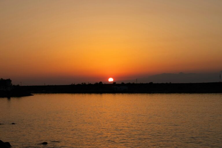 Peaceful beach scene with the sun setting over the horizon, casting warm, calming colors on the water and sand.