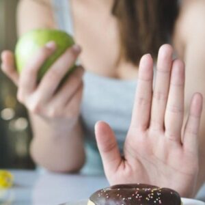 A woman pushing away a sugar donut while holding a fresh apple, symbolizing mindful eating, sugar control, and healthy choices.