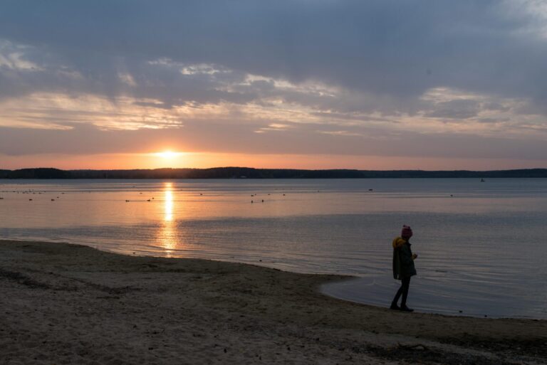 Man standing on the beach at sunset, looking calm and reflective, symbolizing hope and emotional lift.