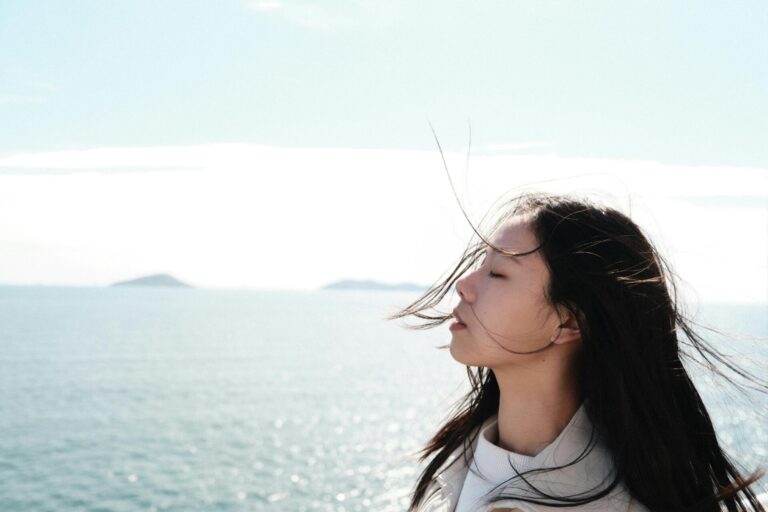 A woman standing calmly with eyes closed, taking a deep breath, symbolizing release, relaxation, and mental freedom.
