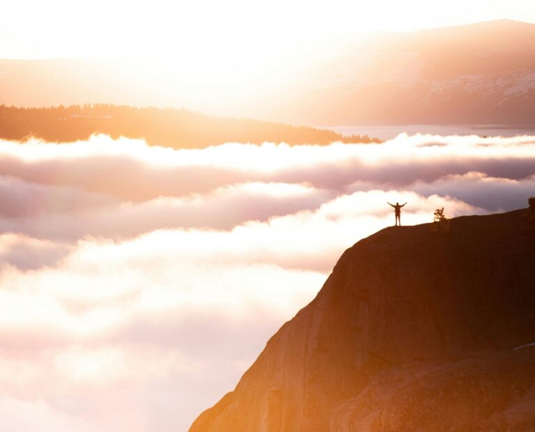 A person standing triumphantly on a mountain peak, arms raised in achievement.