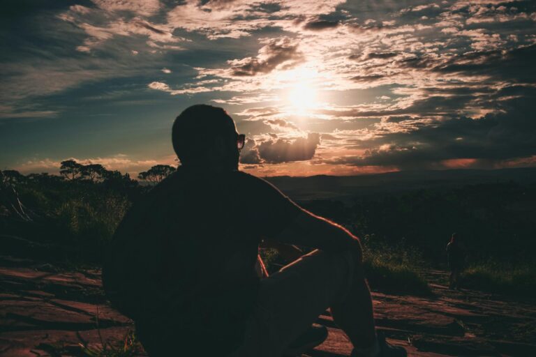 A person sitting peacefully in meditation near a sunrise, symbolizing renewal, healing, and emotional balance through hypnotherapy for addiction.