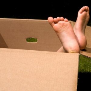 Bare feet sticking out of a cardboard box on the grass.