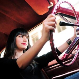A young woman confidently driving a car, hands on the steering wheel.