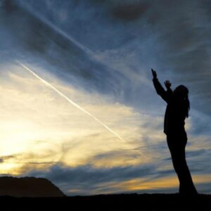A woman standing in front of a sunset, releasing tension and letting go of anger.