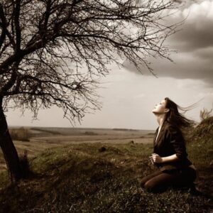 A woman standing by the shore at sunset, gently releasing sadness into the wind.