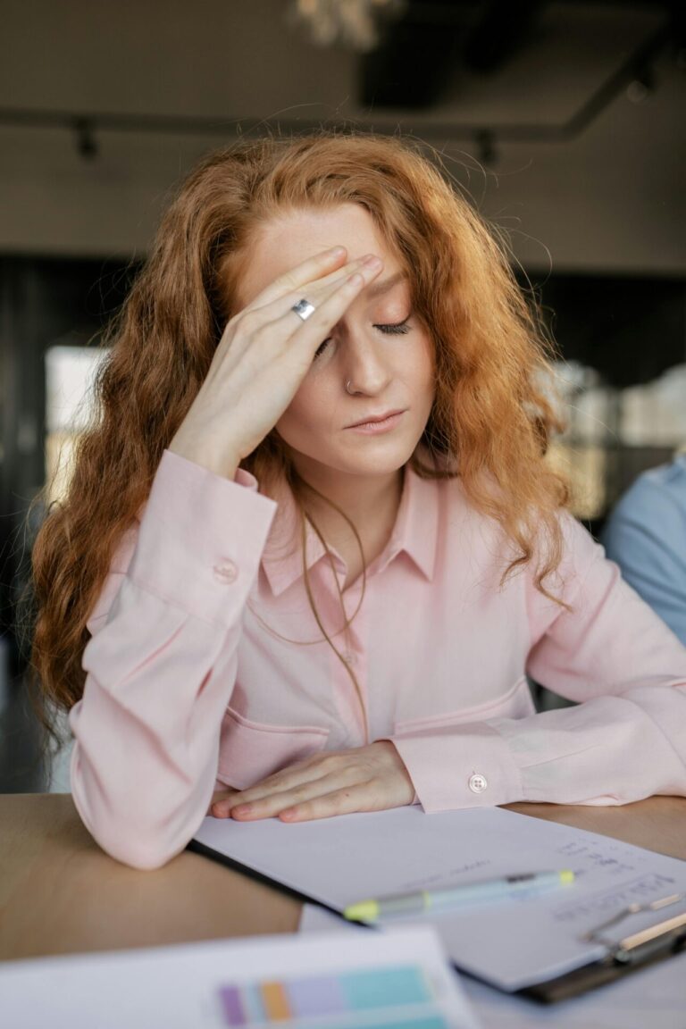 A tired or stressed person sitting at a desk, resting their head on their hand.