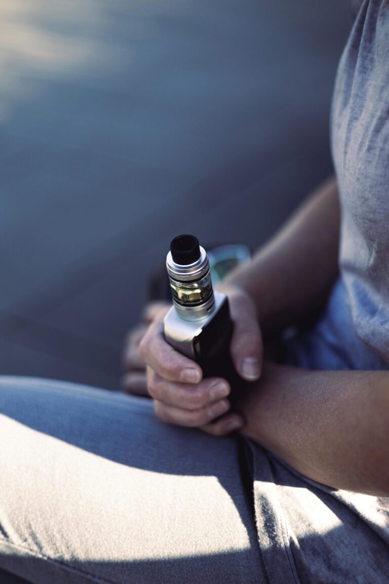 A person holding a vape with smoke rising gently.
