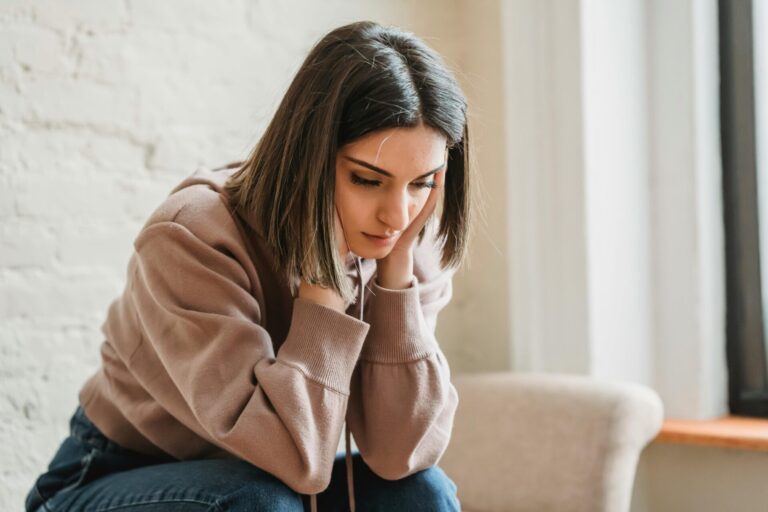 Young woman sitting indoors with her head in her hands, appearing thoughtful or worried.