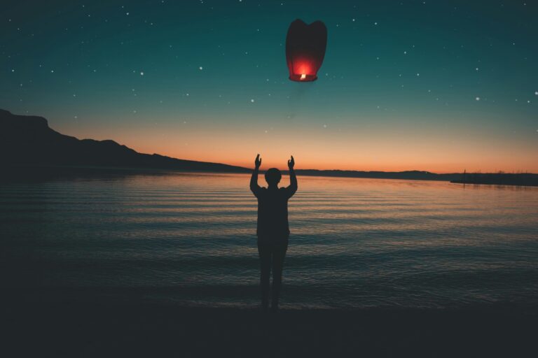 A person releasing a lantern into the sky at dusk, symbolizing letting go and emotional healing.