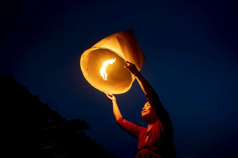 A person holding a glowing lantern, gently releasing it into the night sky.