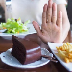 A person raises their hand to refuse chocolate cake and fries, choosing salad instead.