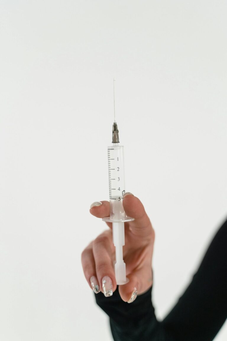 A gloved hand holds a syringe with a needle, preparing for an injection.