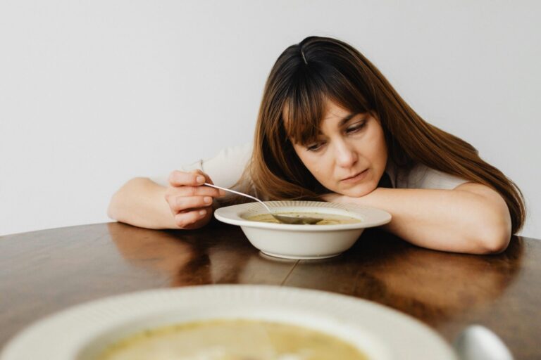 Woman staring at a plate of food with emotional reflection, related to eating habits