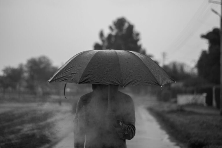 Man standing with an umbrella in a rainstorm, symbolizing emotional protection and shielding from negativity