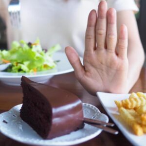 Hand pushing away cakes and sweets to resist compulsive eating urges