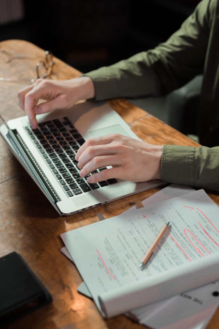 Hands typing on a laptop beside paperwork on a desk